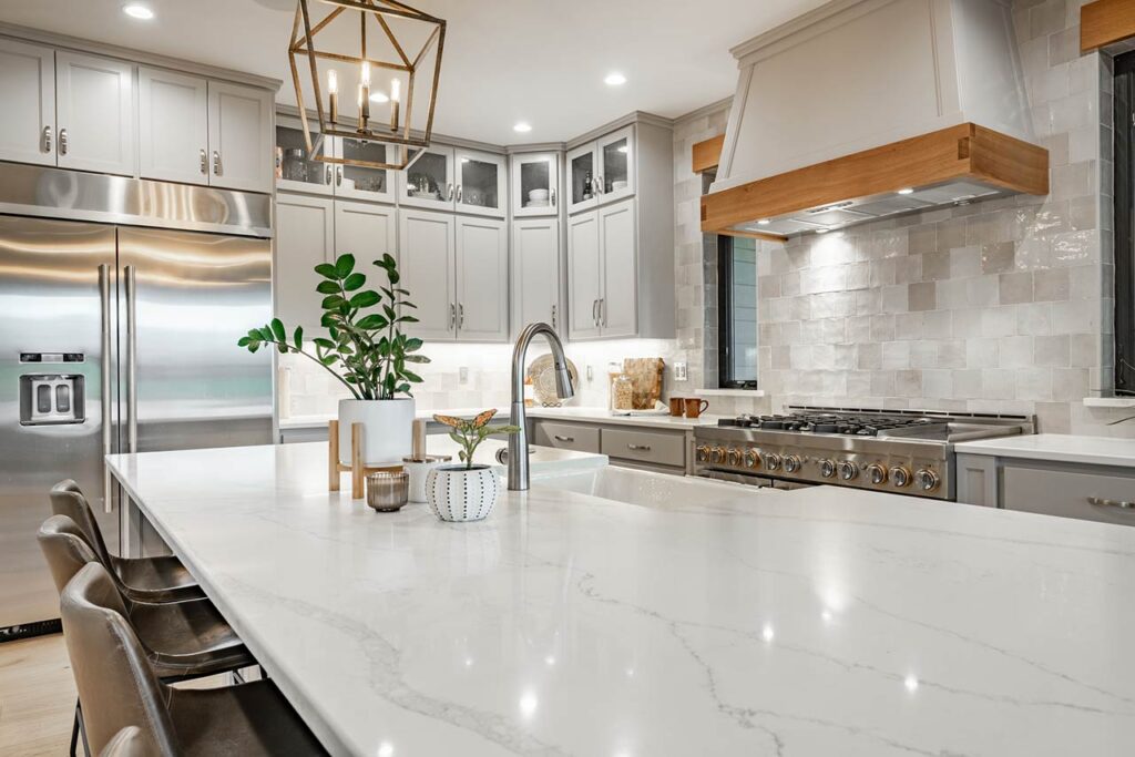 Large kithchen with white countertops, grey cabinets, stainless appliances, large white porcelain double sink farmhouse style